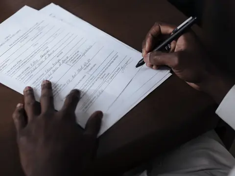A hand filling in a printed form at a desk