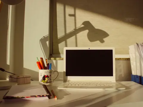 A laptop on a sunlit desk by a window