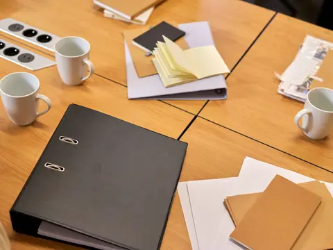 A black binder, notebooks and coffee cups on a wooden table
