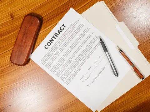 A printed contract, pens and a pen case on a wooden desk