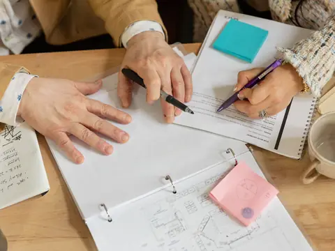 Two people writing notes in a binder beside a cup of tea