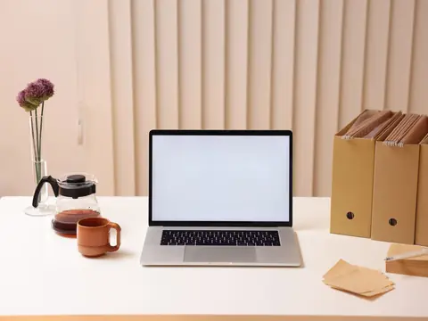 A laptop, a coffee cup and file boxes on a white desk